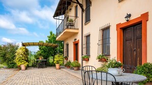 Une cour avec une table et des chaises, entourée de plantes en pot et bordée d’un bâtiment doté d’un balcon.