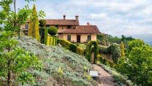 Une villa située sur une colline, avec un chemin de pierre menant à l’entrée, entourée de haies et d’arbustes bien entretenus.