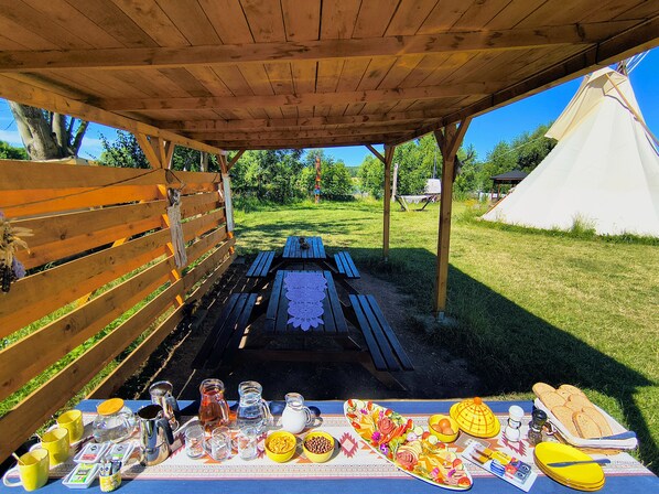 An outdoor picnic setup with a wooden table, benches, and a tent in a grassy area. - Teepee Camp Lounky (Chodouny)