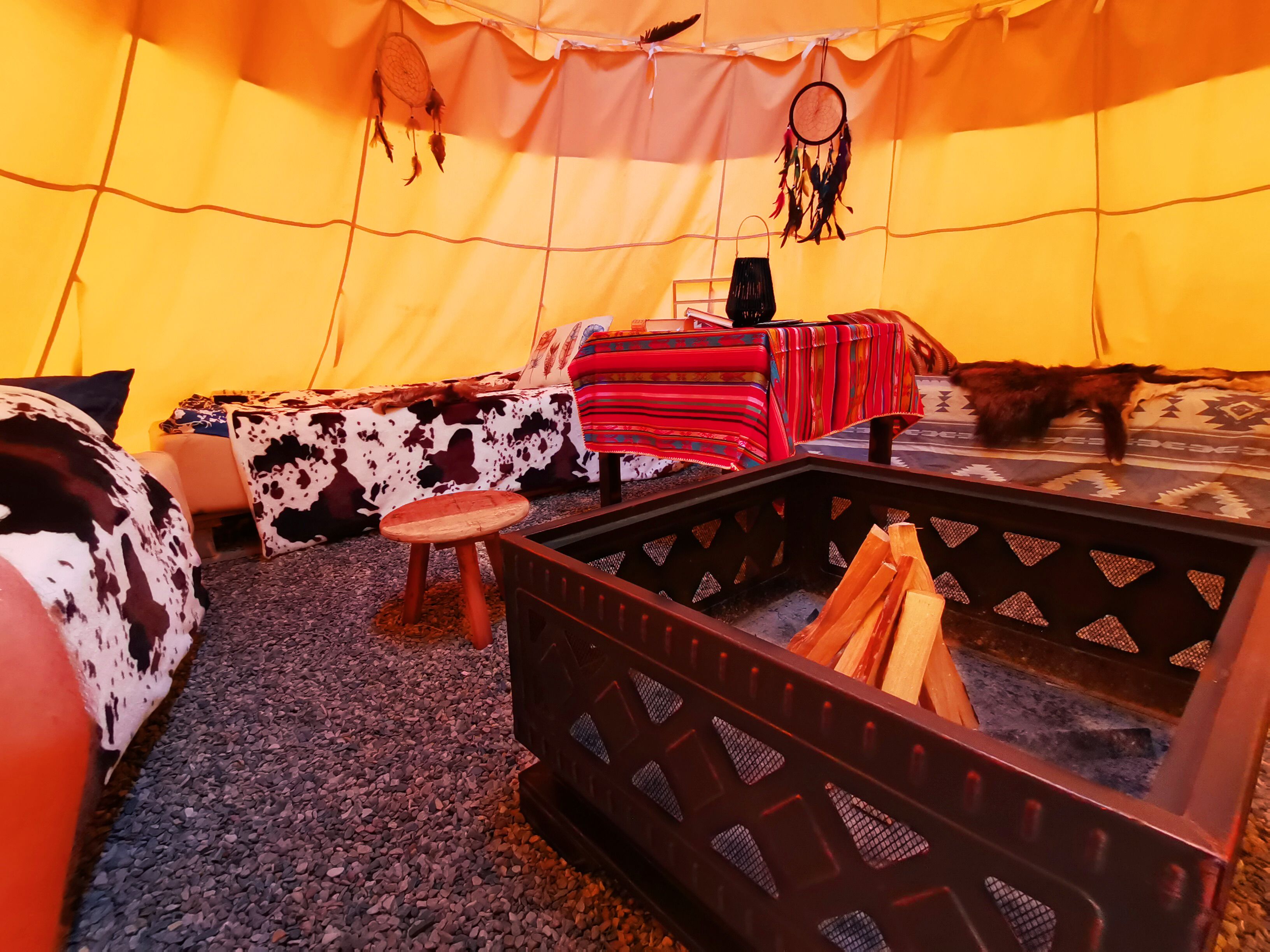 A cozy interior with a bed, a small stool, a fire pit, and a sleeping cat.