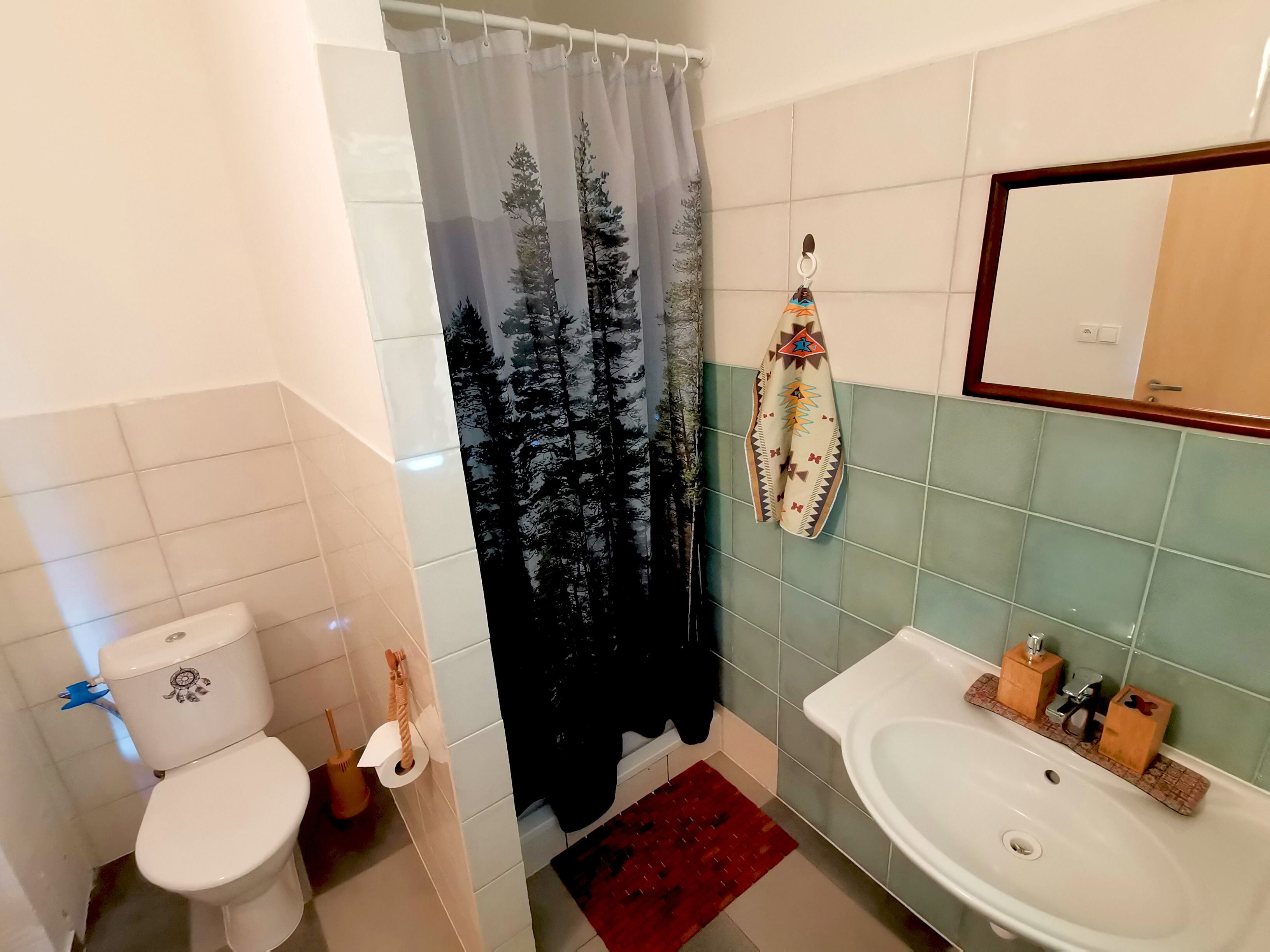 Een badkamer met toilet, wastafel en douchegordijn met een bosmotief.