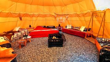 Una tenda con due letti, un tavolino con una bottiglia e una cassa.