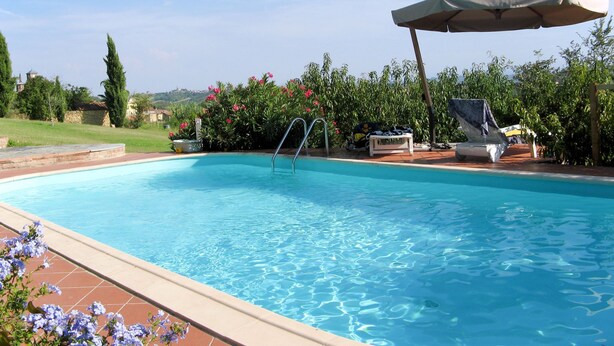 Une piscine aux eaux cristallines, équipée d’un échelle, de chaises longues et d’un parasol.