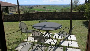 Une terrasse avec une table ronde et quatre chaises, offrant une vue panoramique sur un paysage pittoresque composé de champs et de montagnes lointaines.