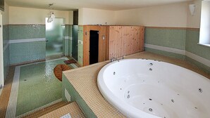 Une salle de bain avec une grande baignoire, un espace douche et une porte en bois.