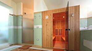 Un sauna aux murs en bois, au sol carrelé et doté d’une porte en verre donnant sur un espace douche.