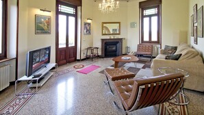 Un salon spacieux doté d’une cheminée, de fauteuils en cuir, d’un canapé, d’une télévision et d’un lustre.