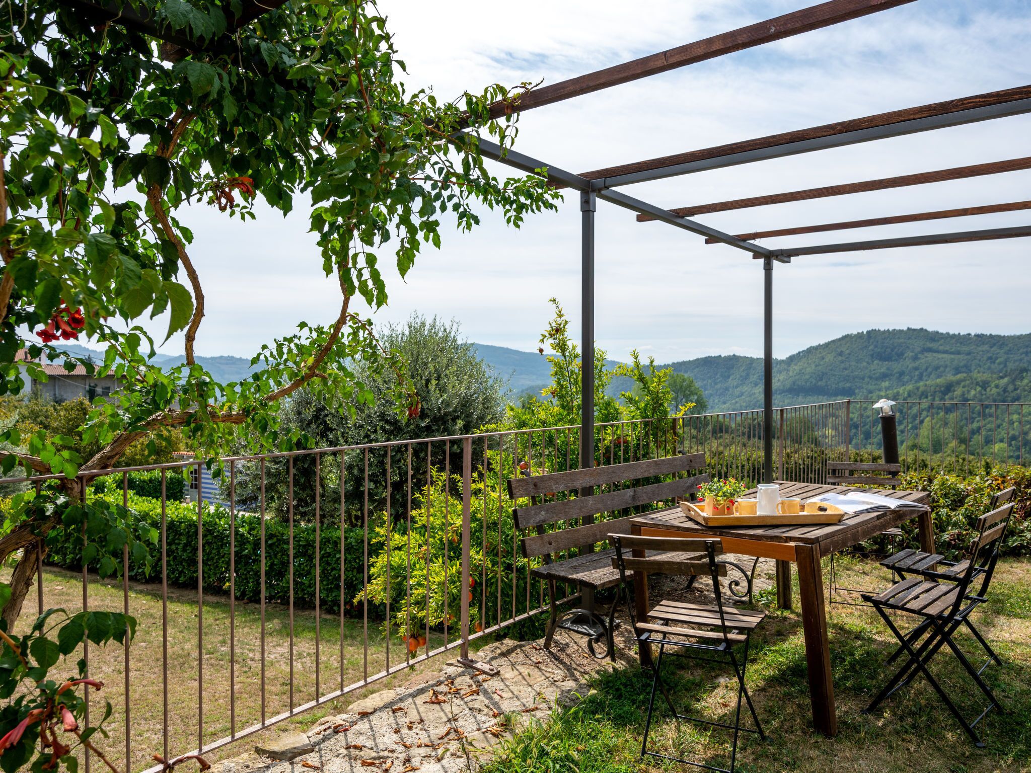 A patio with a table and chairs, surrounded by a metal fence and greenery.