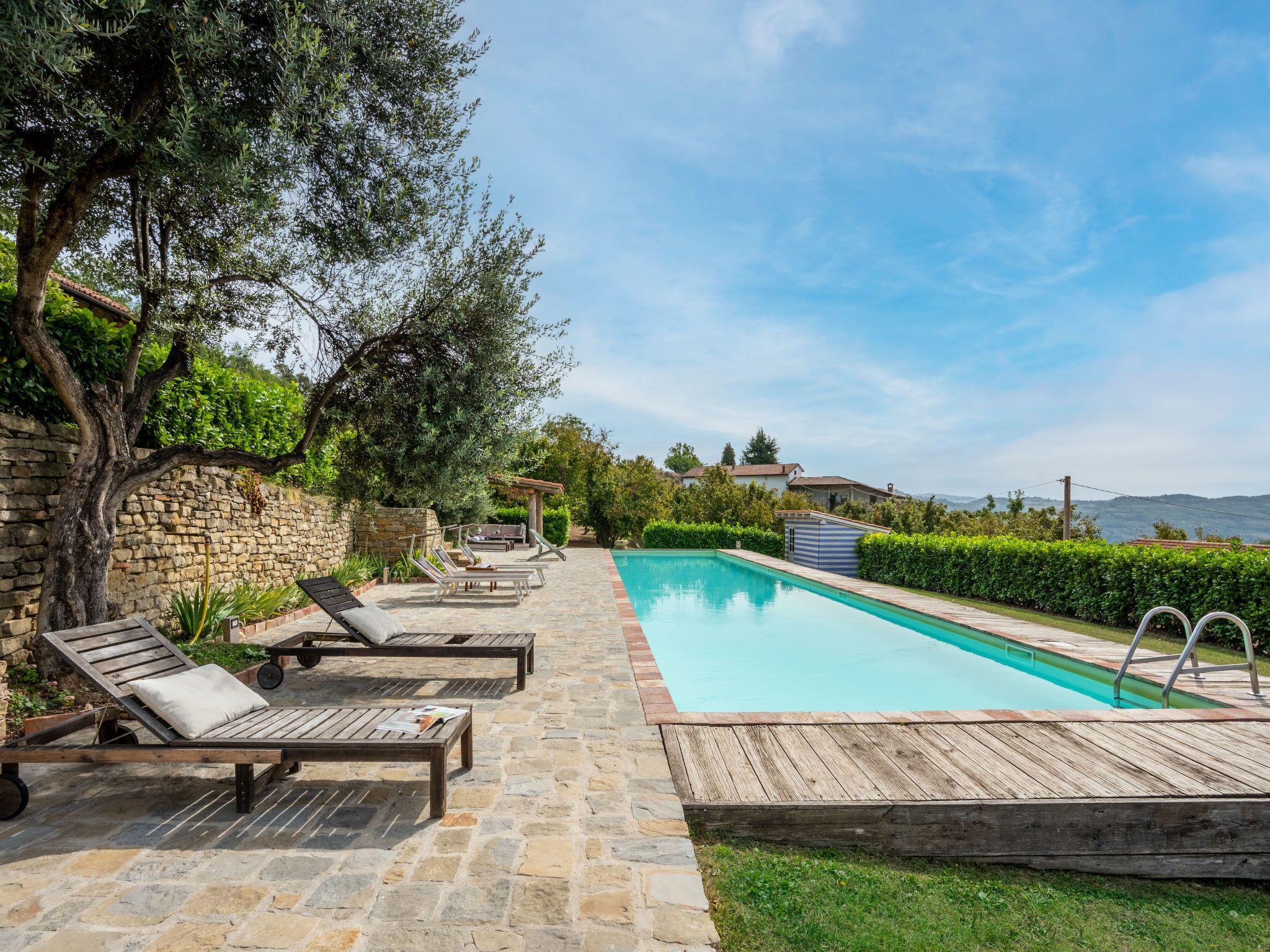 A pool area with lounge chairs, a stone wall, and a view of the landscape.