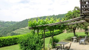 Eine Terrasse mit Tisch und Stühlen, umgeben von üppigem Grün und Blick auf sanfte Hügel.