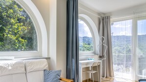 Une pièce moderne avec un banc en bois, un bureau et une chaise. De grandes fenêtres offrent une vue sur la verdure.