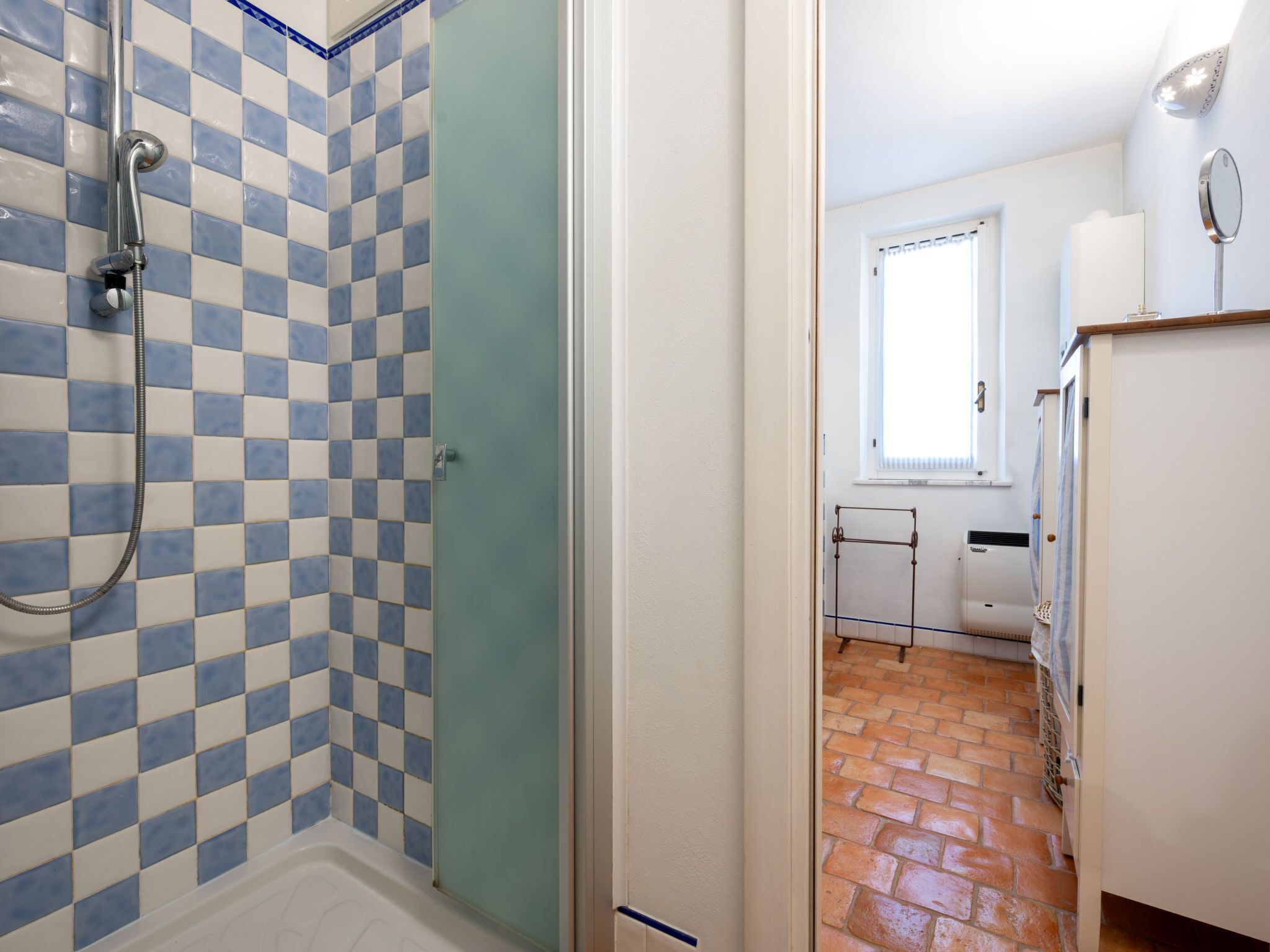 Um banheiro com parede de azulejos quadriculados, chuveiro e janela com persianas.