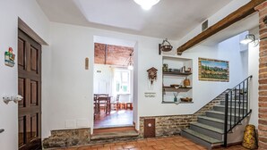 Ein geräumiger Korridor mit Fliesenboden, einer Holztür, einer Treppe mit Metallgeländer und einer rustikalen Ziegelwand.