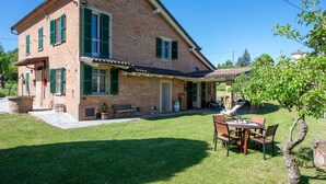 Ein zweistöckiges Backsteinhaus mit grünen Fensterläden, einer Terrasse mit Gartenmöbeln und einem kleinen Garten.