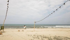 Ein Strand mit einer Reihe von Lichterketten, einigen Liegestühlen und ein paar Personen in der Ferne.