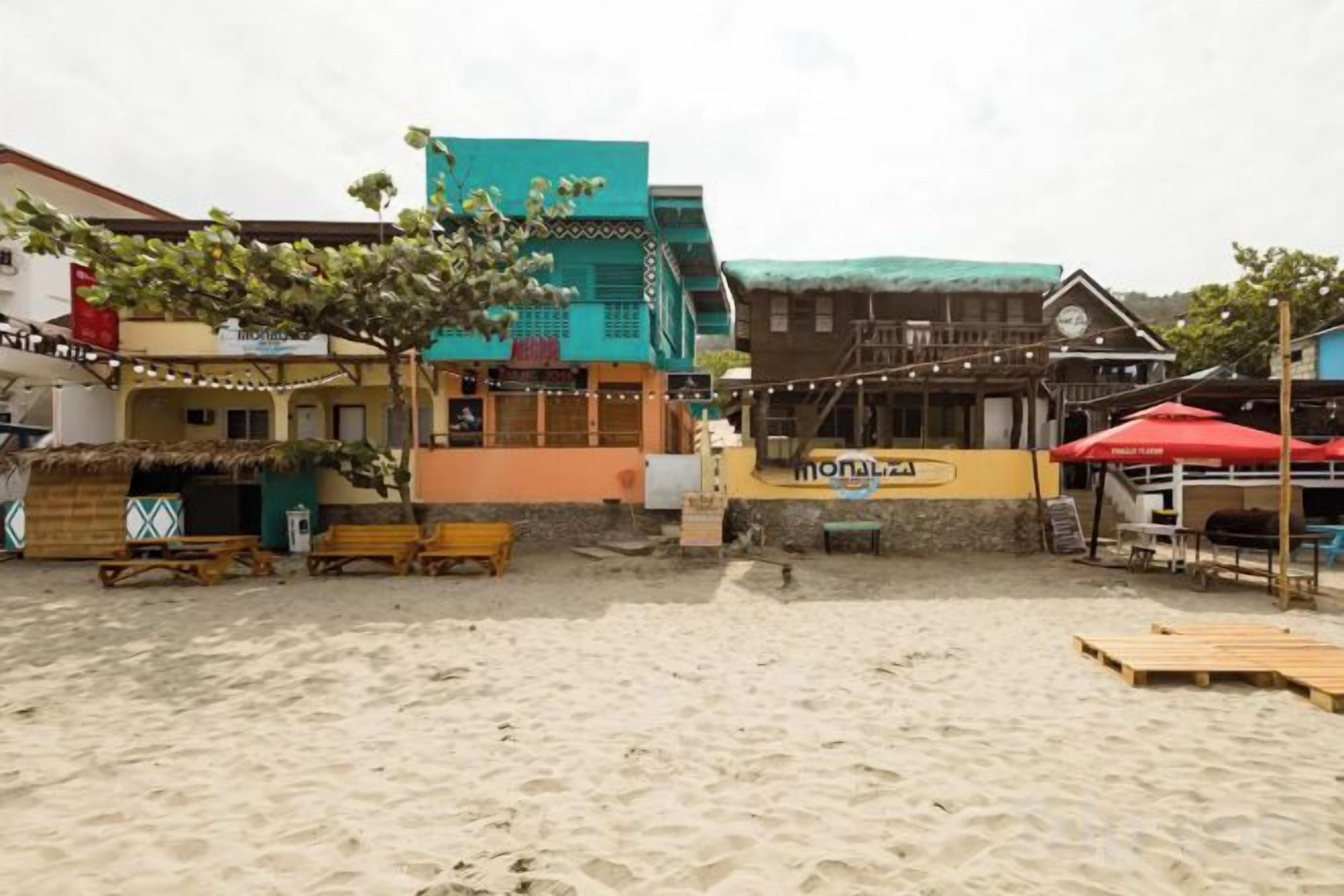 A beachside area with a wooden deck, lounge chairs, and a building with a green roof.
