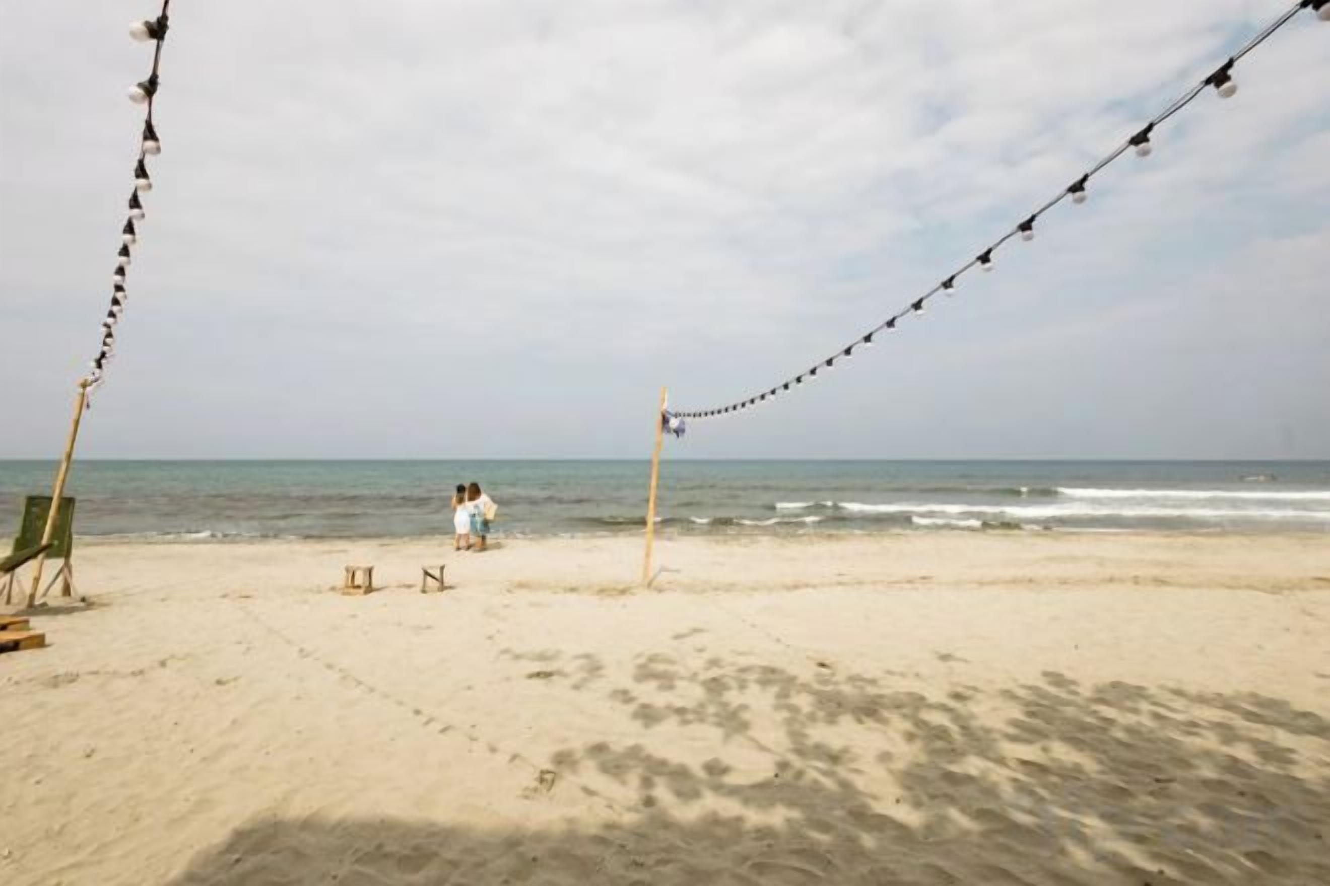 A beach with a string of lights, a chair, and a table.