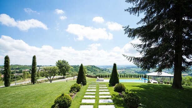 A well-maintained garden with a stone pathway leading to a pool area, surrounded by neatly trimmed hedges and trees. - Villa Loreto by Interhome (Costigliole d'Asti)
