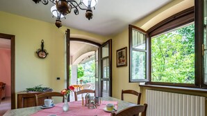 Zona de menjador amb taula preparada per a quatre, cadires, un candelabrum, un rellotge i una finestra amb vista a vegetació.