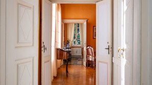 Un pasillo con suelo de madera, puertas blancas y un ventanal con cortinas.