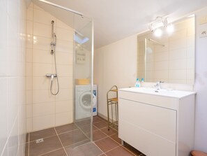 A modern bathroom with a glass-enclosed shower, a white sink with a mirror, and a washing machine in the background. - Vacation home Magali by Interhome (Hyères)