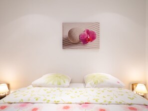 A neatly made bed with floral bedding, two pillows, and a wall-mounted picture of an orchid and sand. - Vacation home Magali by Interhome (Hyères)