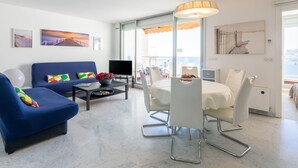 A modern living room with a blue sofa, a dining table with white chairs, a TV, and artwork on the walls. - Parc Massolin by Interhome (Roquebrune Cap Martin)