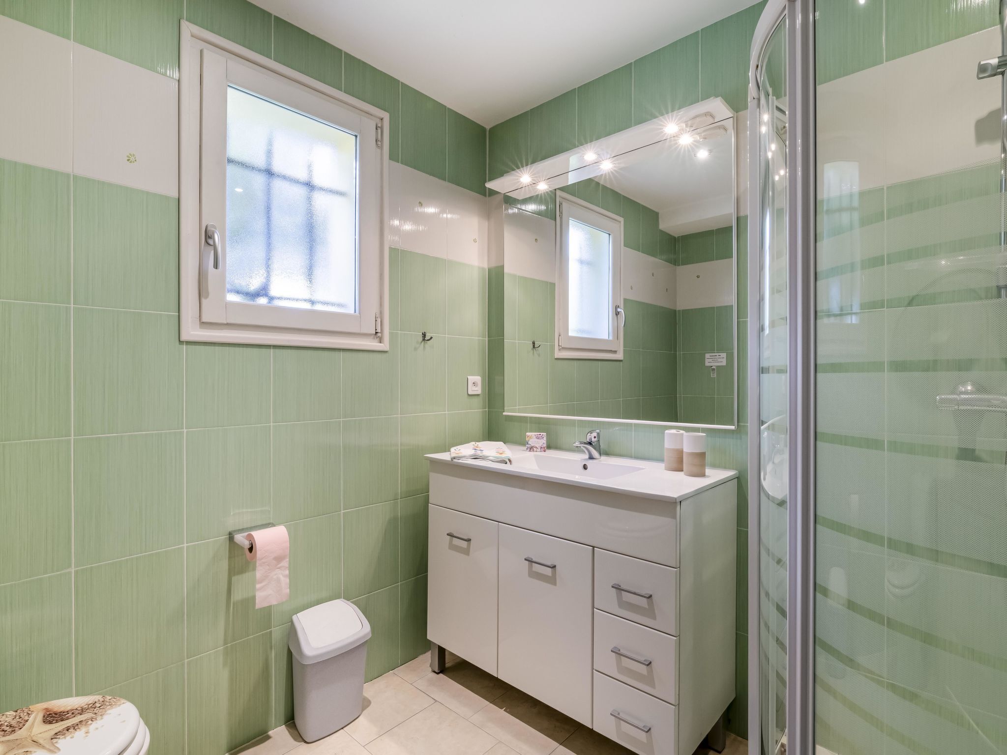 A bathroom with green tiles, a white sink, a mirror, and a shower.