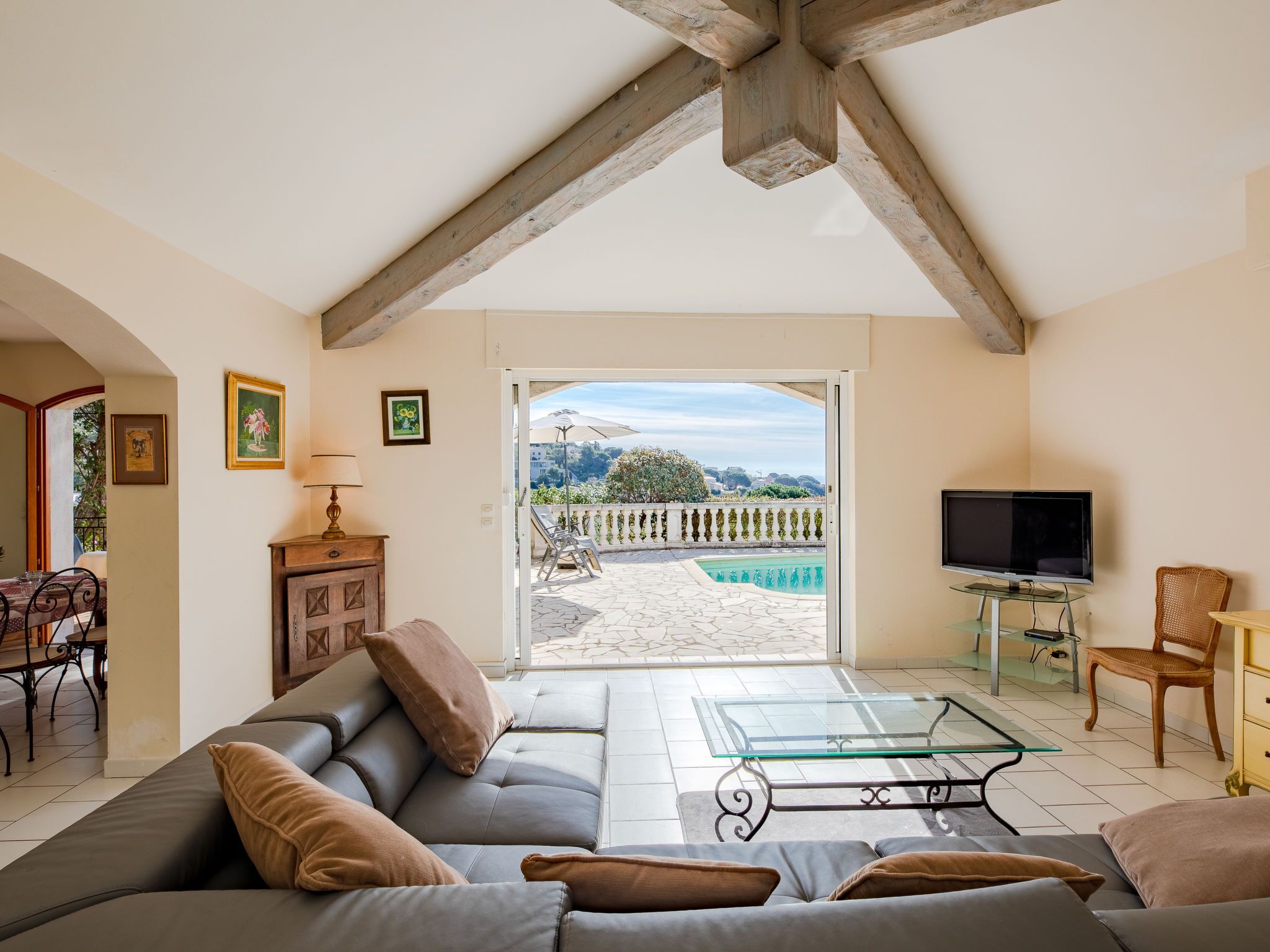 Ein Wohnzimmer mit Sofa, Glastisch, Fernseher und Blick auf Pool und Garten.