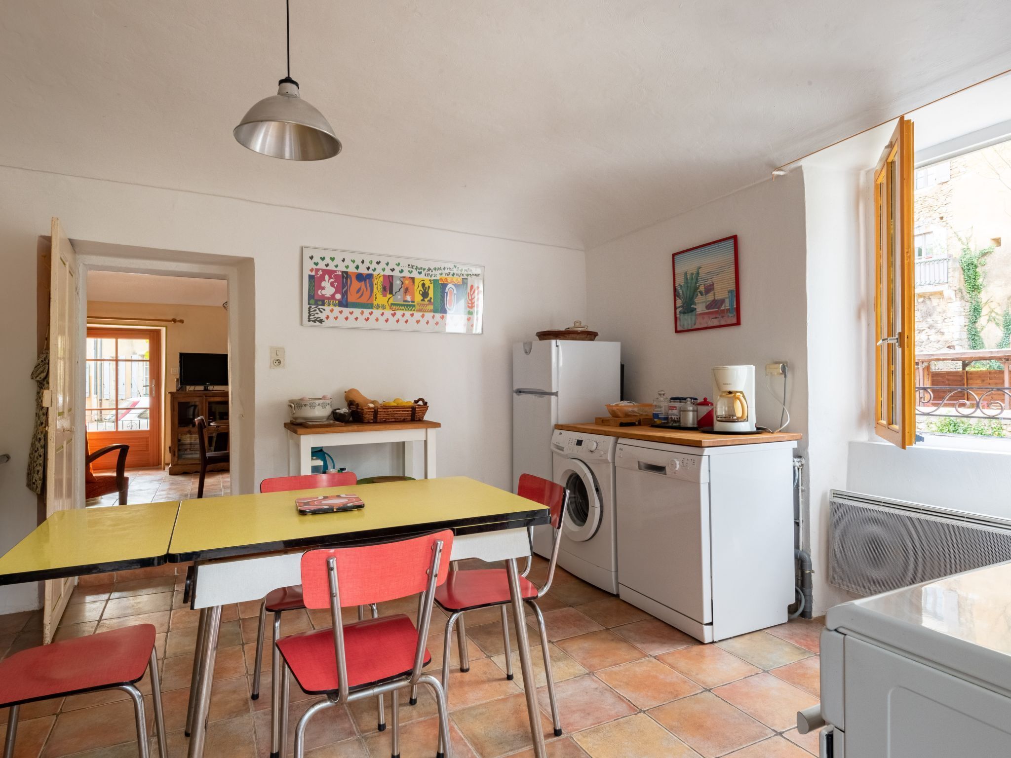 A compact kitchen with a washing machine, a dining table with chairs, and a hanging light fixture.