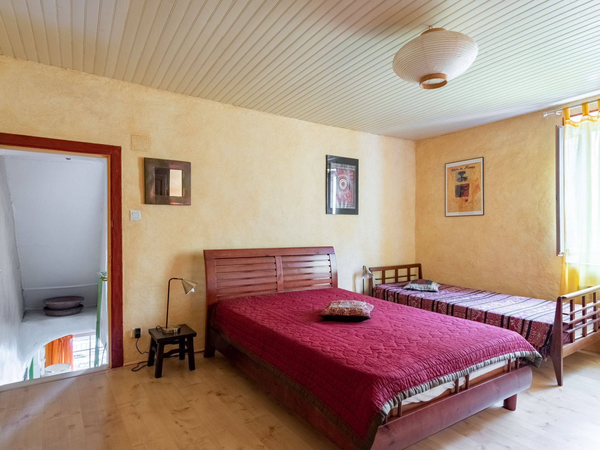 A bedroom with a large bed, a smaller bed, a desk, and a chair. There are two framed pictures on the wall.