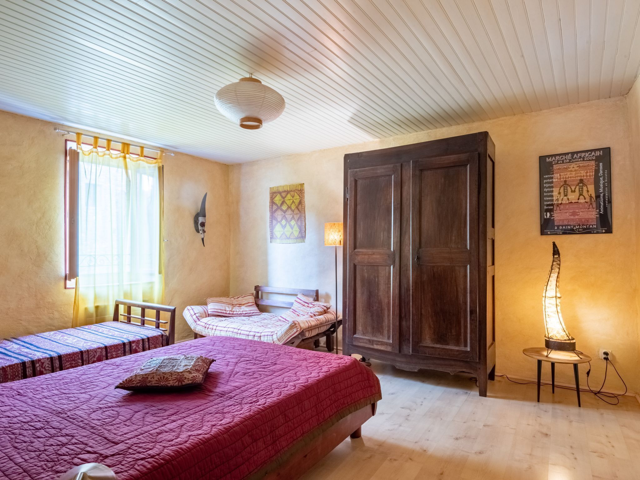 A room with two beds, a wooden wardrobe, a wall-mounted lamp, and a decorative wall hanging.