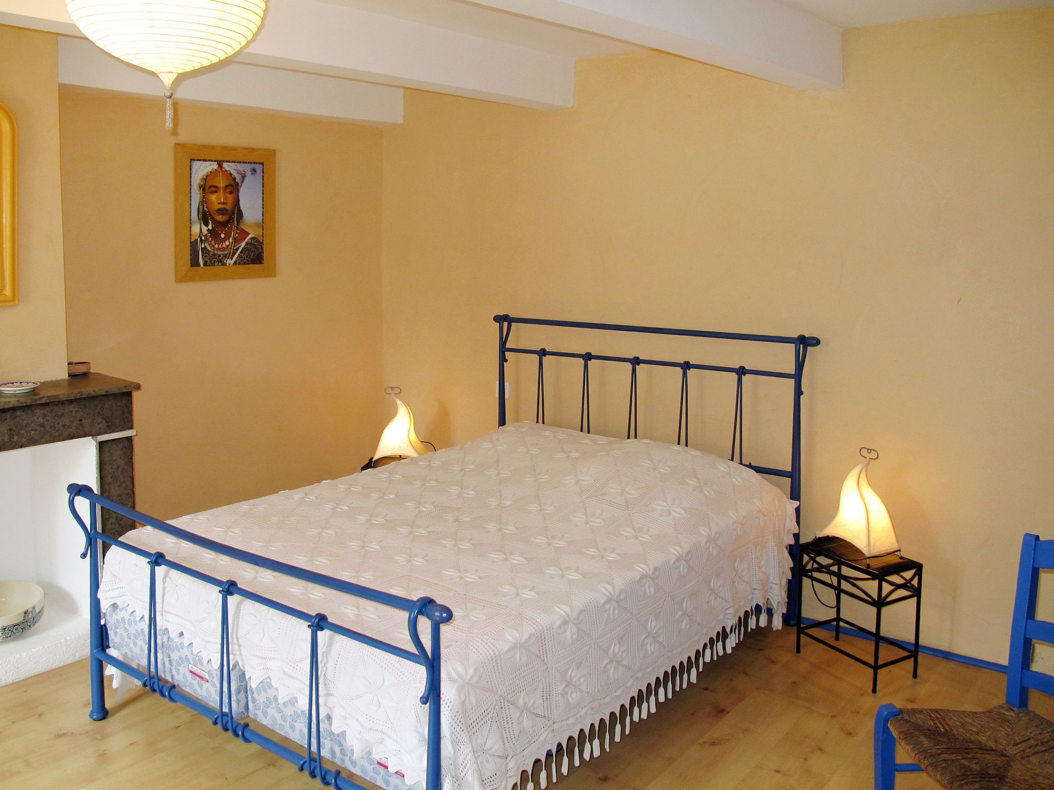 Een slaapkamer met een bed, nachtlampjes, een stoel, een klein tafeltje en een schilderij aan de muur.