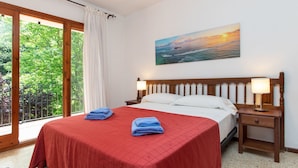 Ein Schlafzimmer mit einem großen Bett, zwei Nachttischen, einem Fenster mit Blick auf Grünflächen und einem Gemälde von einem Sonnenuntergang.