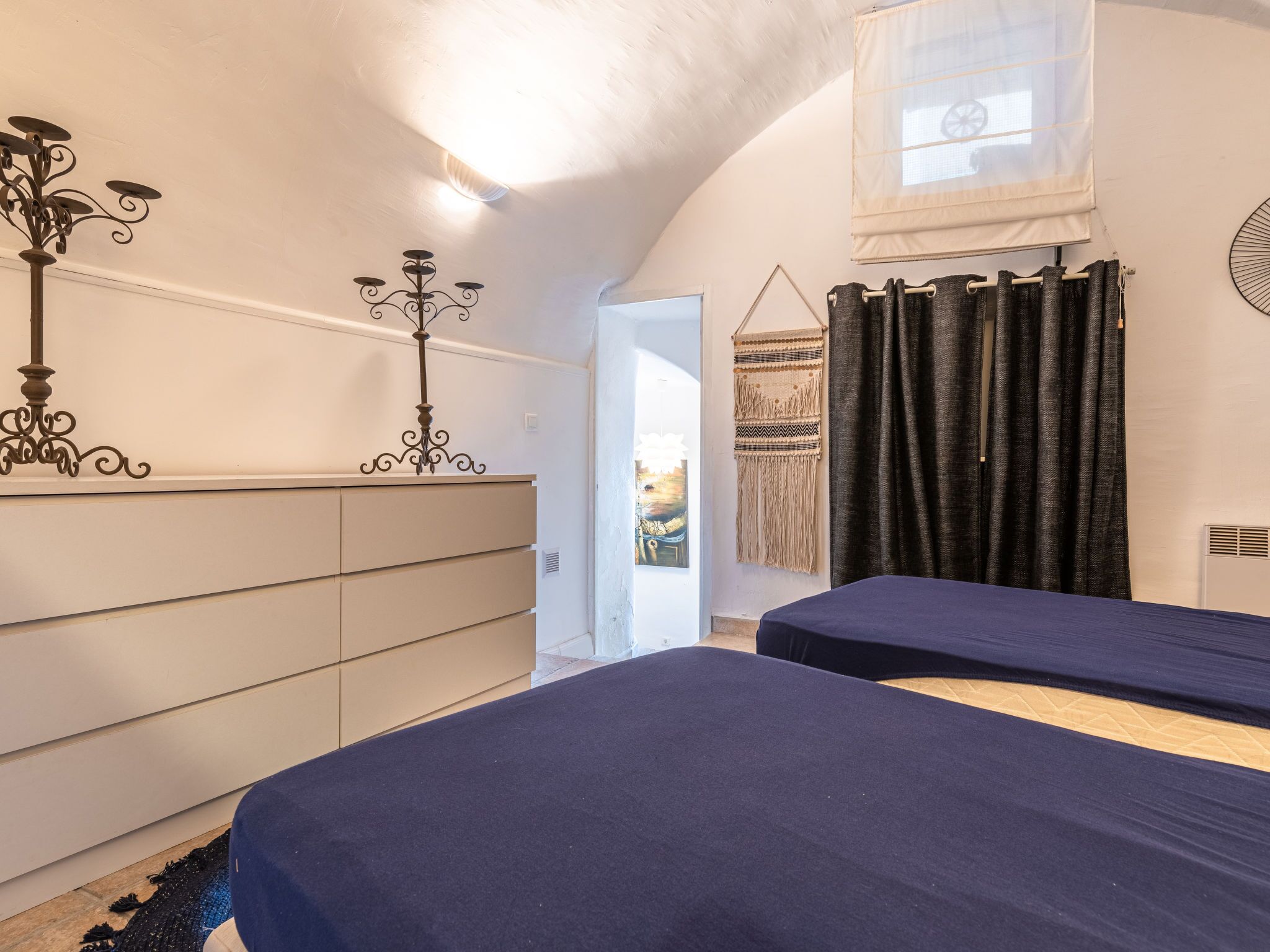 A bedroom with two beds, a dresser, a chandelier, and a window with curtains.