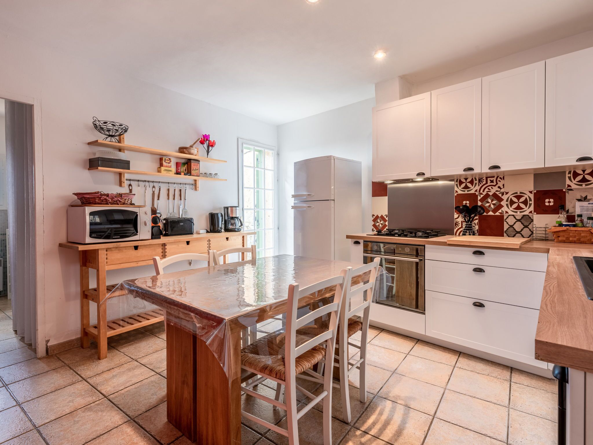 A modern kitchen with white cabinets, a wooden dining table, and a built-in oven.