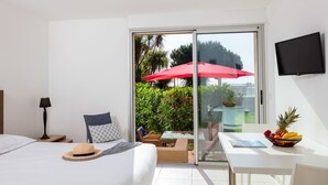 A hotel room with a bed, a desk, a TV, and a sliding glass door to a balcony with a red umbrella. - MB2 sans vue mer by Interhome (Moriani-Plage)