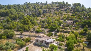 Une maison en pierre, avec un toit de tuiles, entourée d’arbres et située dans un paysage vallonné.