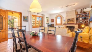 A dining area with a wooden table and chairs, a chandelier, and a bookshelf with books and decorative items. - Sa Caseta by Interhome (Muro)