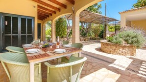 An outdoor dining area with a wooden table and wicker chairs, surrounded by stone flooring and greenery. - Sa Caseta by Interhome (Muro)
