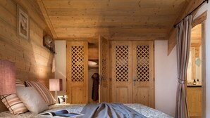 A wooden bedroom with a bed, a nightstand, a lamp, and a wardrobe with a lattice design.
