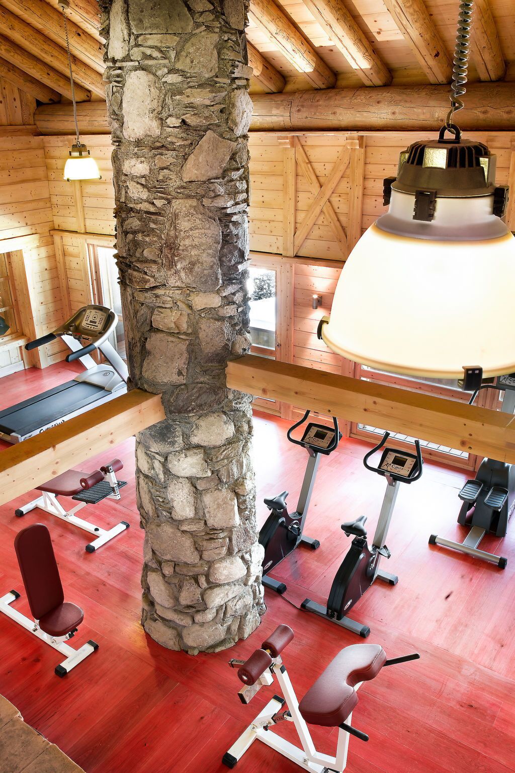 A gym with exercise equipment, a stone pillar, and wooden beams on the ceiling.