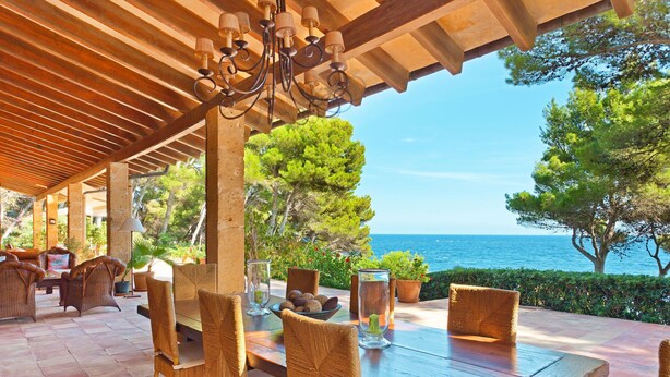 Une terrasse extérieure aménagée avec des meubles en osier, une table en bois et une vue sur la mer.