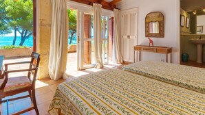 Une chambre avec deux lits, un plafond en bois, une vue sur la mer et une salle de bain équipée d’un lavabo et d’un miroir.