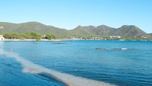 Une vue sur la côte, avec une eau limpide, une plage de sable et, en arrière-plan, des collines verdoyantes.