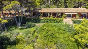 Une villa de style méditerranéen, dotée d’un toit recouvert de tuiles en terre cuite, entourée d’une végétation luxuriante et de pins.