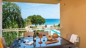 Un balcone con tavolo in vetro, sedie in vimini, una bottiglia di vino, bicchieri, un cestino di pane e un cappello.
