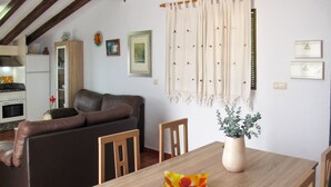 A cozy living area with a sofa, a dining table, and chairs. There is a vase with flowers on the table.