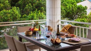 A dining table set with food, drinks, and wicker chairs on a balcony with a view of trees and mountains.