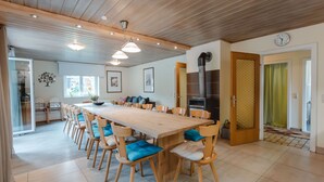 Een ruime eethoek met een lange houten tafel en meerdere stoelen, een moderne keuken met een inbouwoven, en een groot raam dat zorgt voor natuurlijk licht.